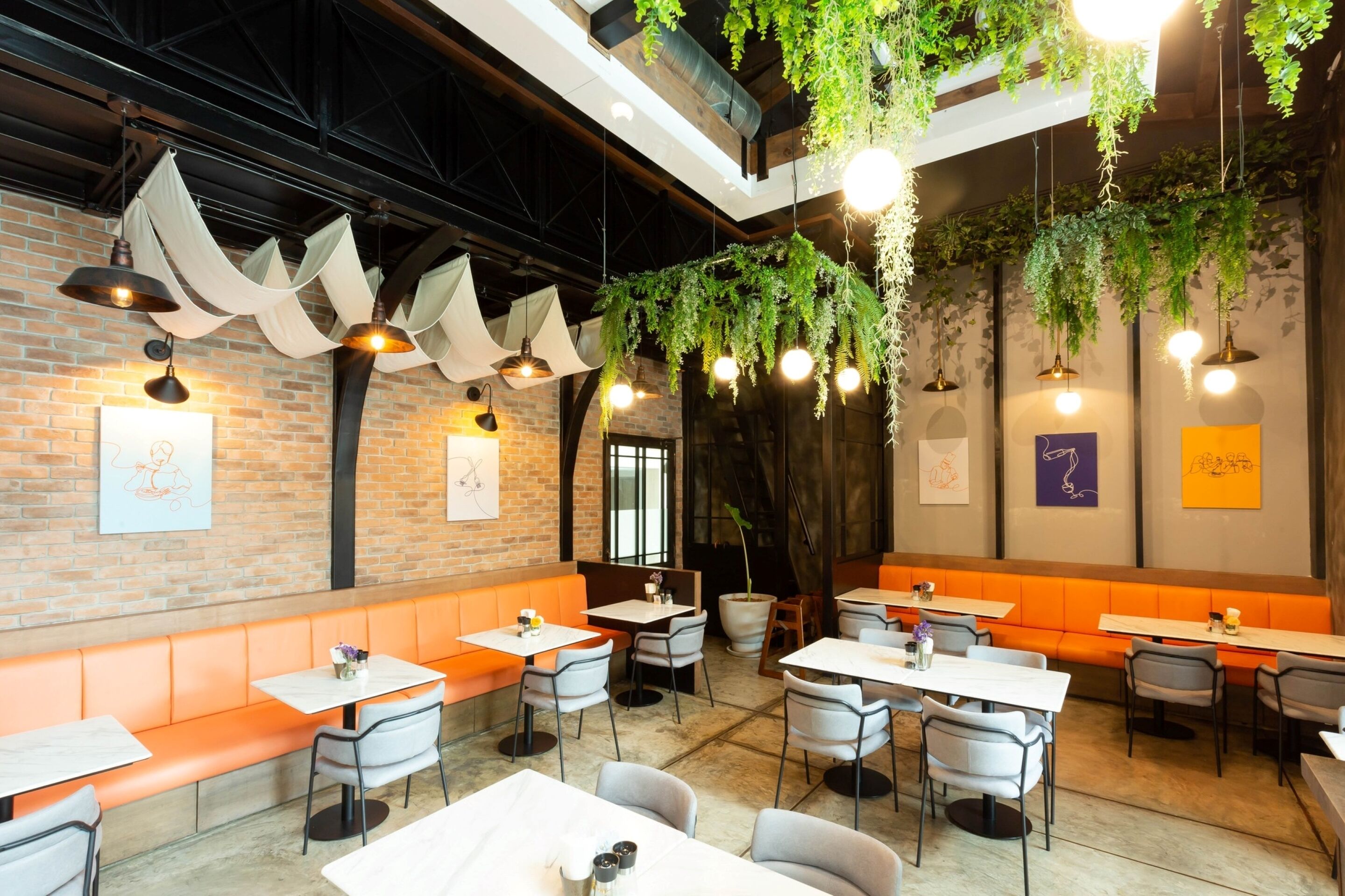 Interior de restaurante con paredes de ladrillo, asientos color naranja, plantas colgantes e iluminación colgante.