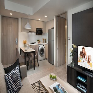 Een modern appartement met keuken, eethoek en woonkamer. Het is voorzien van een wasmachine, een koelkast, een eettafel met stoelen, een bank en een flatscreen-televisie.