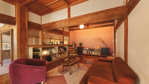 A spacious living room with a wooden ceiling, a purple armchair, a brown sofa, a coffee table, and a bookshelf filled with books and decorative items. - Kominka Yado LOOF Sakanoie (Fuefuki)