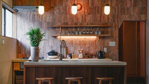 A kitchen with wooden paneling, a central island with stools, and hanging pendant lights. - Kominka Yado LOOF Sakanoie (Fuefuki)