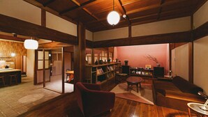 A spacious living area with wooden floors, a red sofa, a round coffee table, and a bookshelf. - Kominka Yado LOOF Sakanoie (Fuefuki)