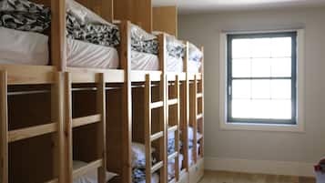 Quarto com beliches, janela e piso de madeira.