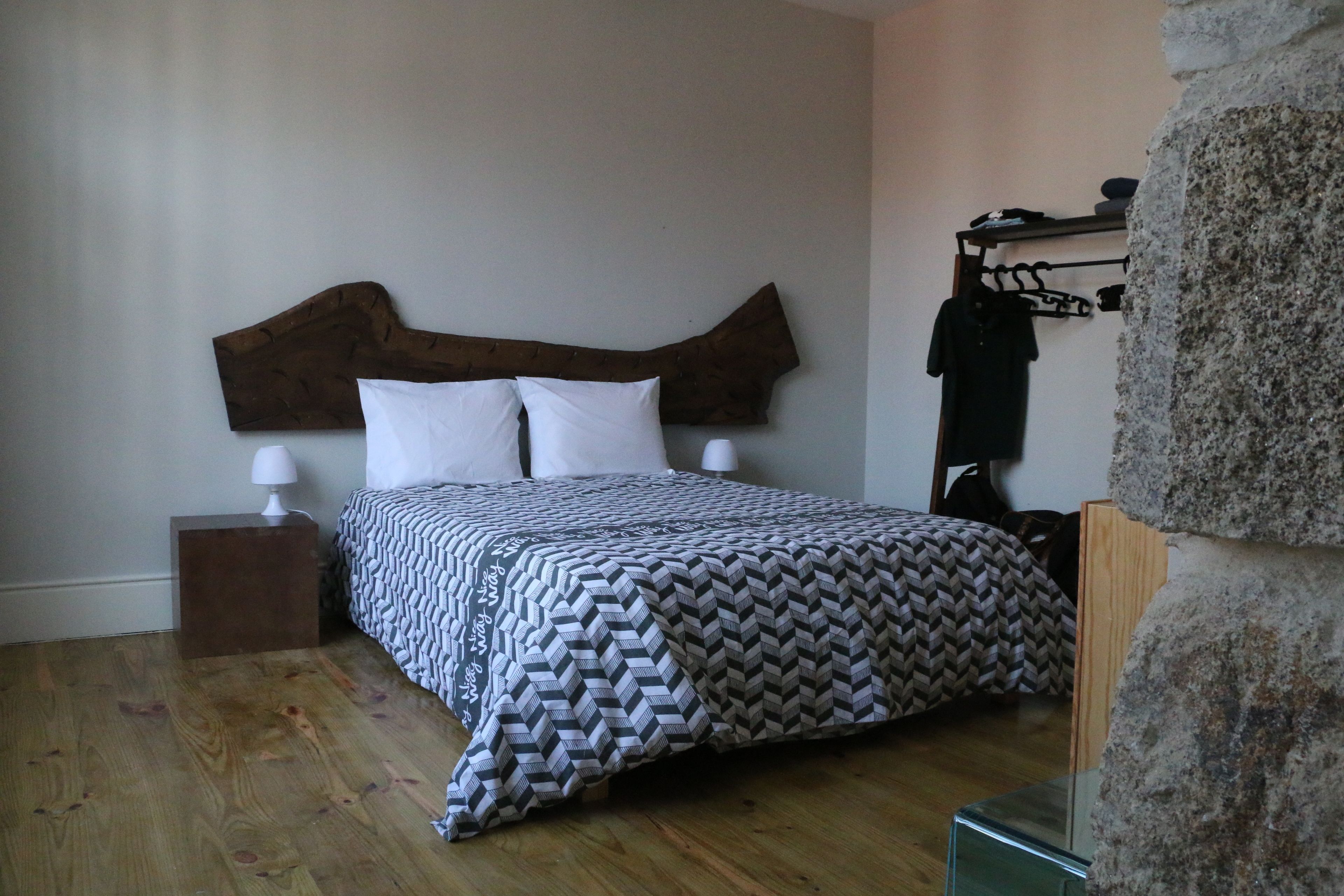 A bedroom with a wooden headboard, a patterned bedspread, a nightstand with a lamp, and a stone accent wall.