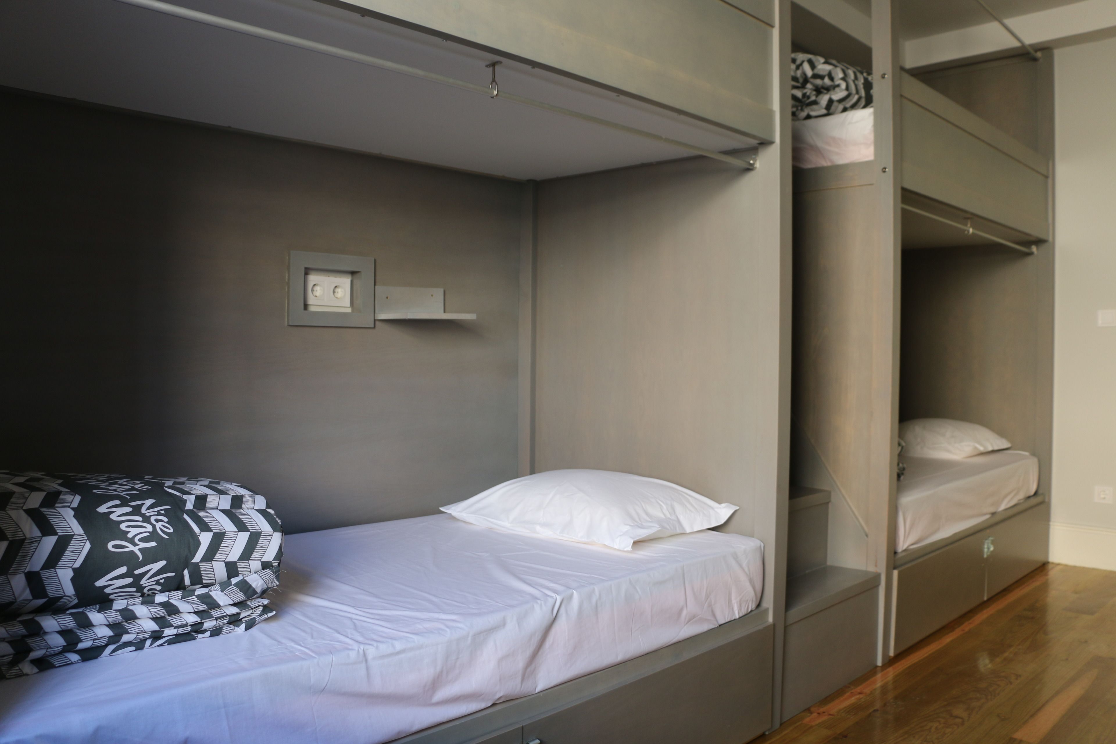 Habitación con literas, un colchón blanco, una almohada estampada y un interruptor de luz en la pared.
