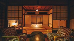 Habitació japonesa tradicional amb sòl de tatami, sostre de fusta baix i portes corredisses shoji. Al primer pla, hi ha dues cadires amb dibuixos de llebrer i una taula petita.