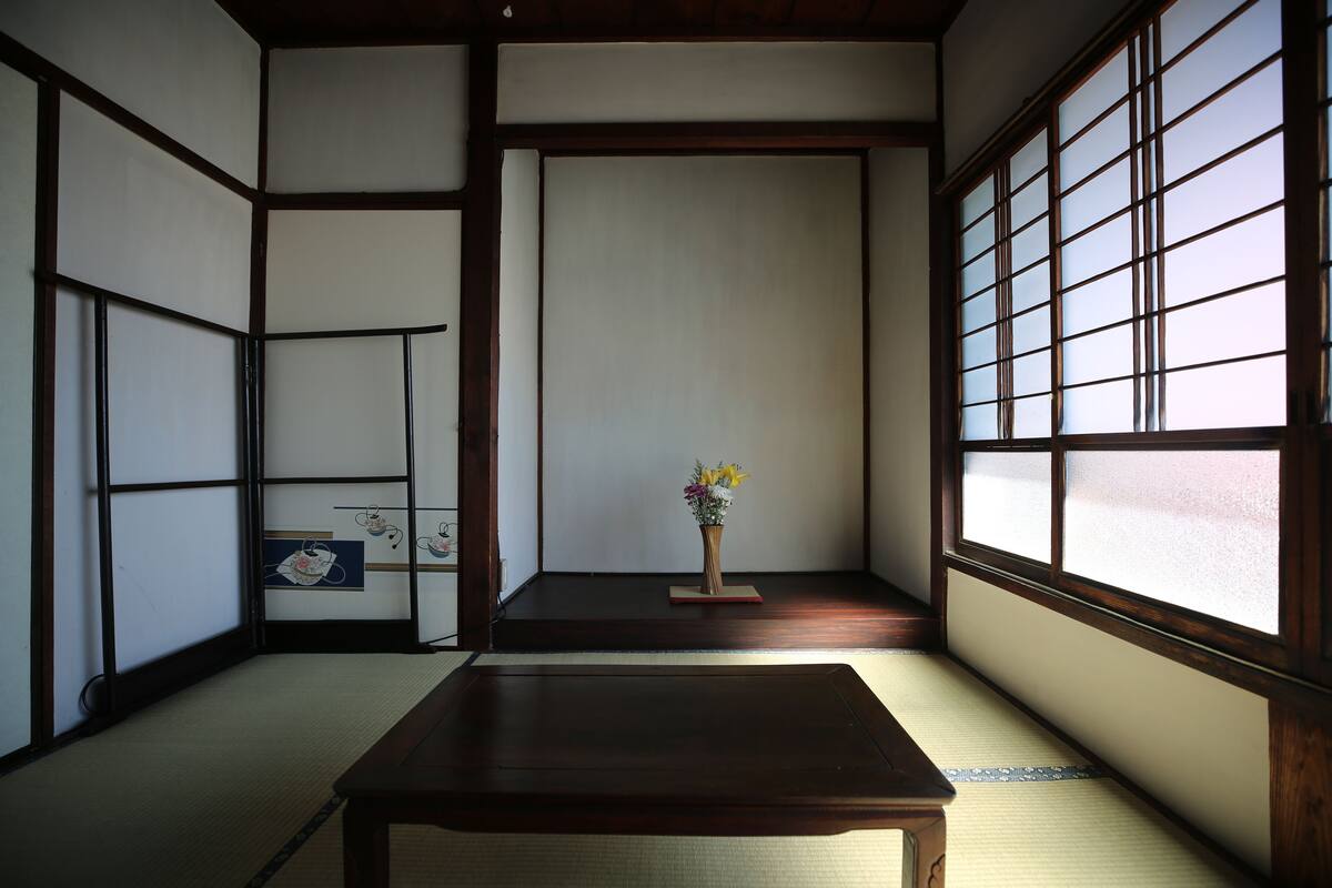 A traditional Japanese room with tatami flooring, a low wooden table, a vase with flowers, and shoji screens.