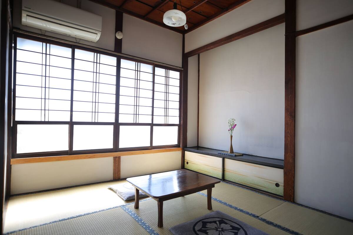 A traditional Japanese room with tatami flooring, a sliding door, a small wooden table, and a vase with flowers.