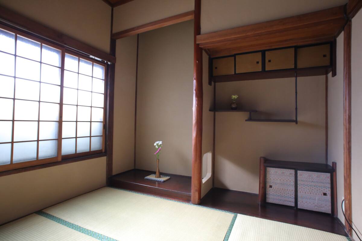 A traditional Japanese room with tatami flooring, a shoji screen, a small wooden shelf with a vase, and a sliding door.