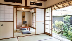 Habitació japonesa tradicional amb terra de tatami, una taula de fusta baixa, una televisió i vistes a un jardí.