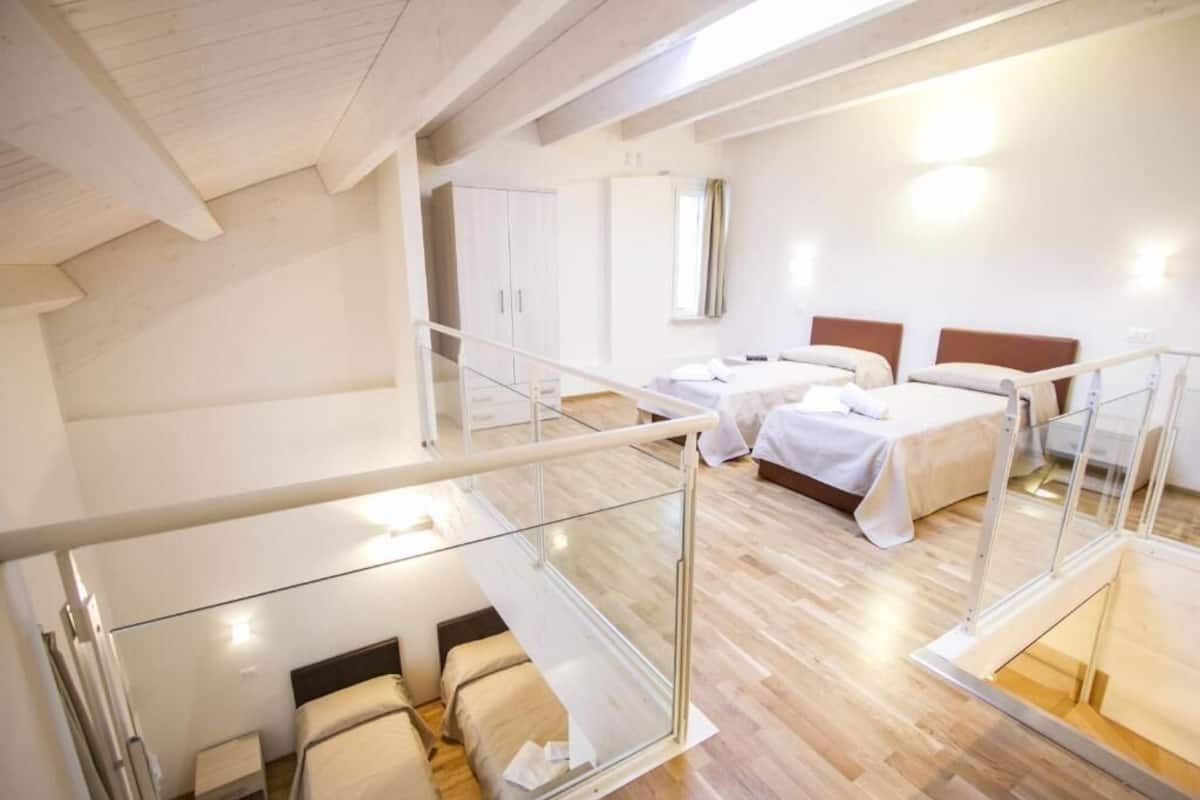A modern hotel room with a glass balcony, two beds, a wardrobe, and a large mirror.