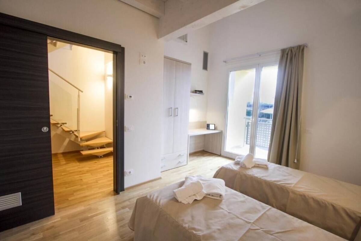 A hotel room with a bed, a desk, a window with curtains, and a staircase leading to another room.