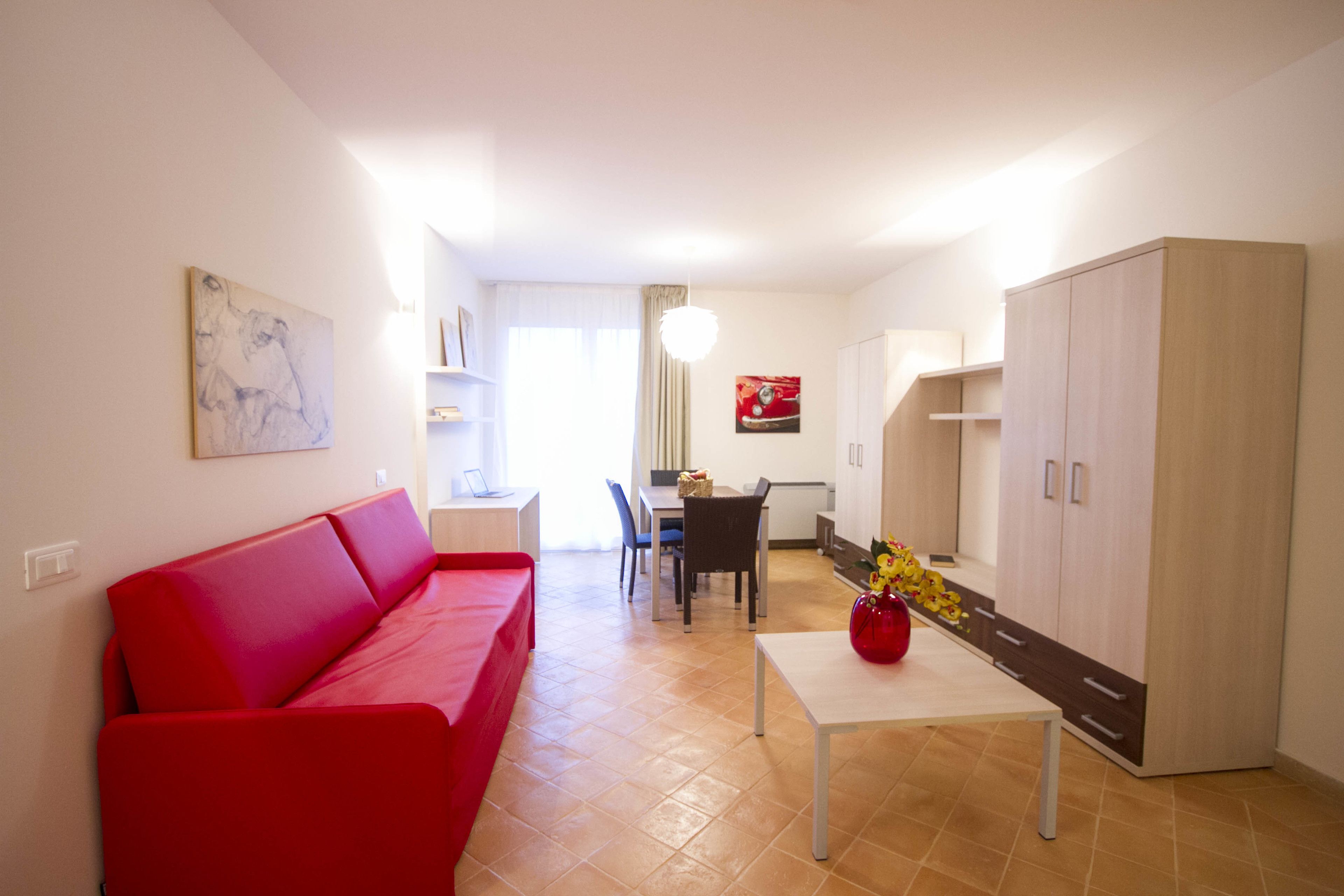 Una sala de estar moderna con un sofá rojo, una mesa de comedor con sillas, una zona de cocina y un armario.