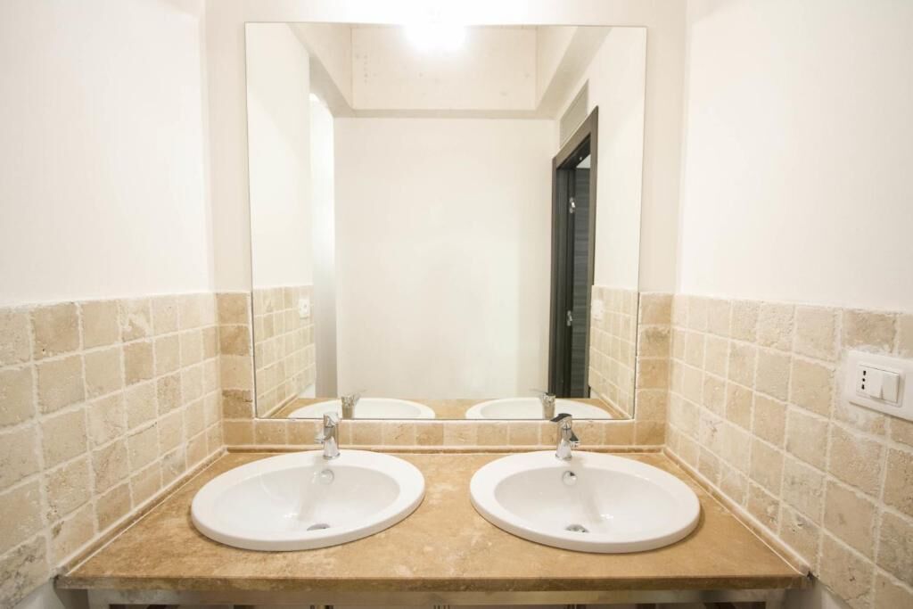 A bathroom with two sinks, a large mirror, and beige tiled walls.