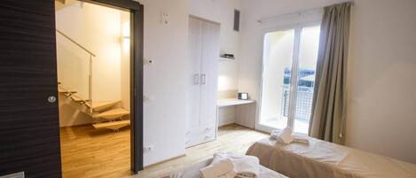 A hotel room with two beds, a balcony with a view, a staircase, and a wardrobe.