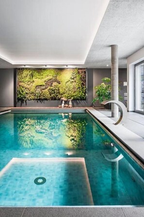 A modern indoor pool with clear water, a textured wall behind, and a minimalist design. - Hotel Wellness Eau de Roche (Durbuy)