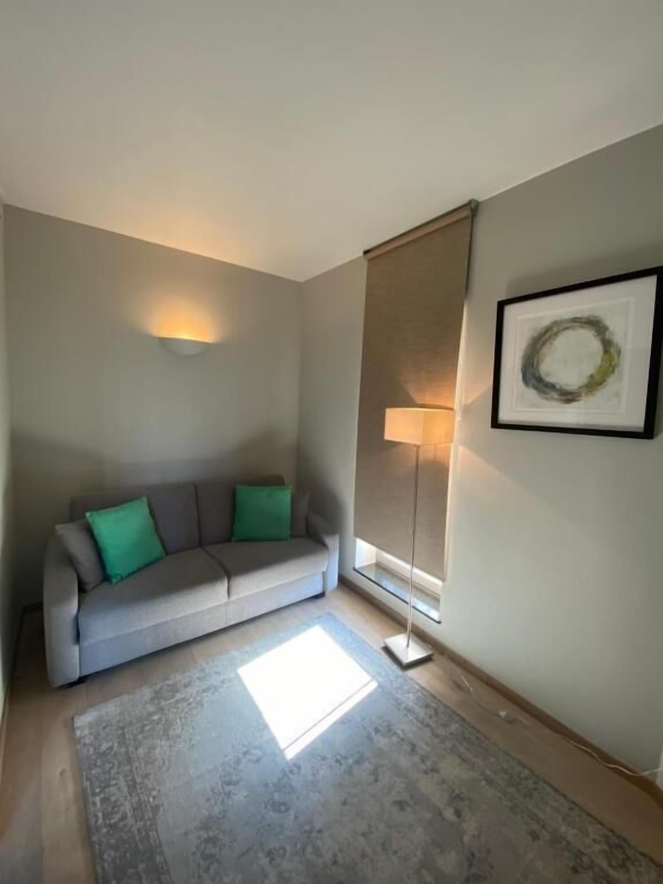 A living room with a grey sofa, a floor lamp, and a framed artwork on the wall.
