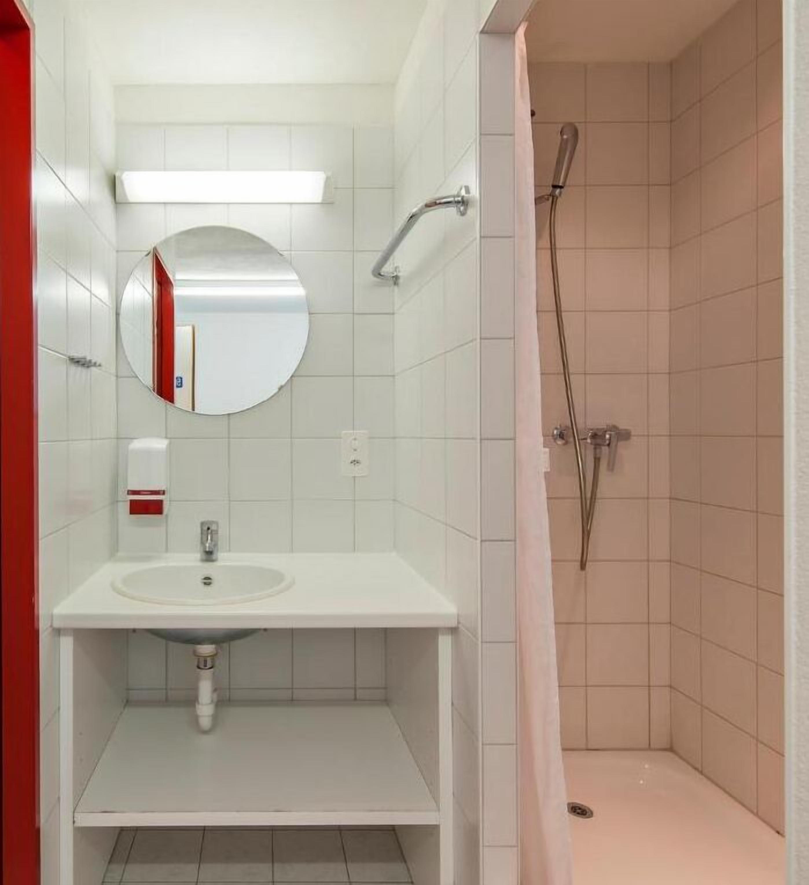 Een badkamer met een wit wastafelmeubel, spiegel en douche.
