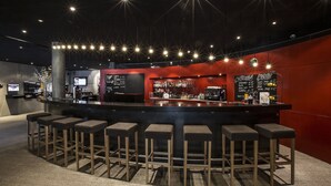 Un área de bar moderna con un mostrador central, varios taburetes y una pizarra de menú.