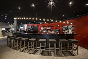 Un área de bar moderna con un mostrador central, varios taburetes y una pizarra de menú.