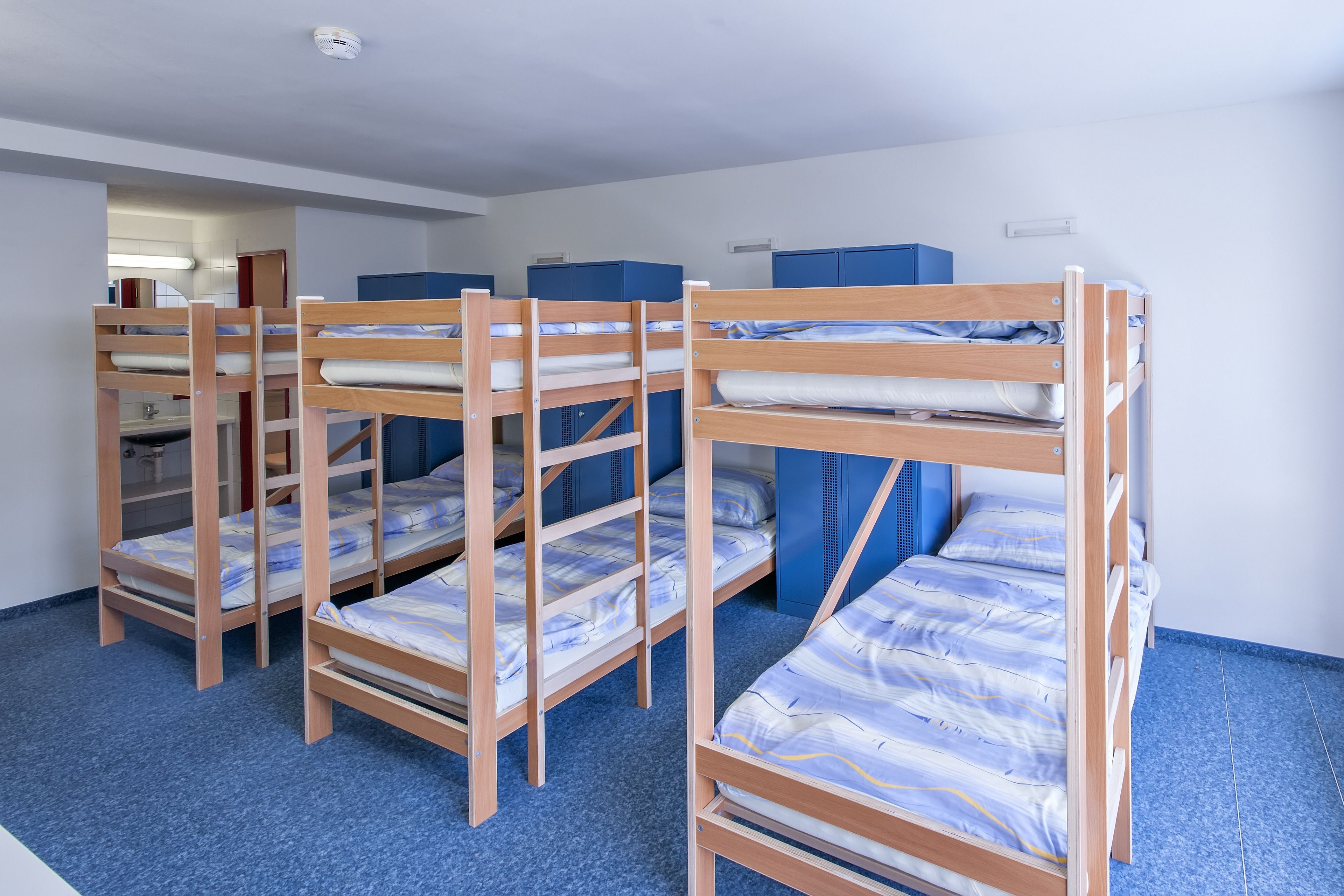 Ein Schlafsaalzimmer mit Stockbetten, blauen Stauraumbereichen und einem blauen Teppich.