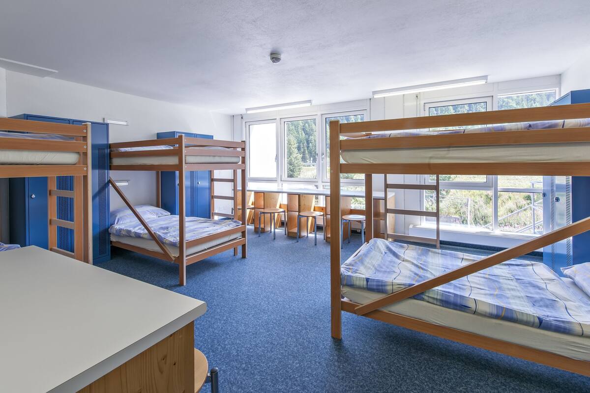 Een studentenkamer met stapelbedden, een bureau en een raam met uitzicht op de omgeving.