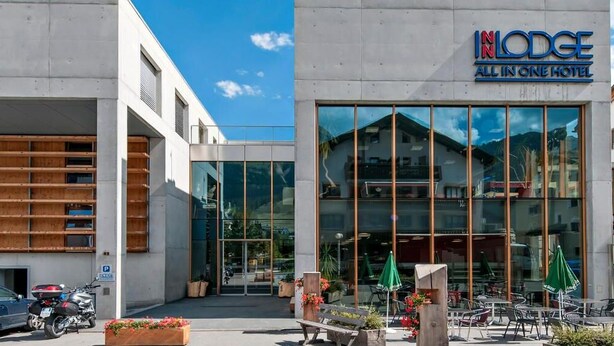 Un hotel moderno con fachada de vidrio, asientos al aire libre y vistas a la montaña.