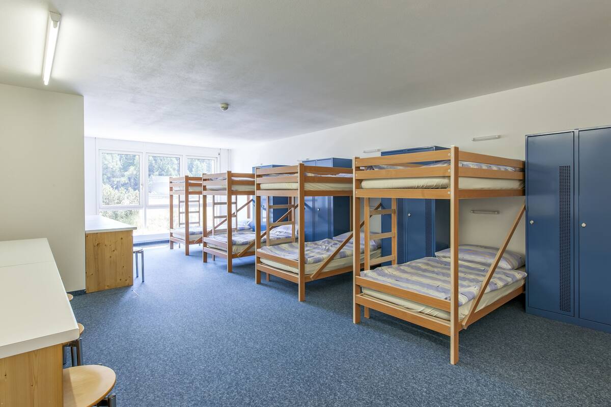 Een studentenkamer met stapelbedden, een bureau en een raam.