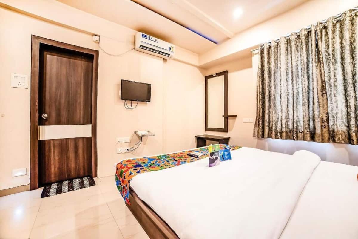 A hotel room with a bed, a television, an air conditioning unit, a door, and a curtain.