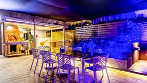 An outdoor dining area with a brick oven, wooden slats, and blue ambient lighting. - FabHotel Imperio (Pune)