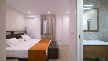 A modern hotel room with a large bed, a bench, a bathroom with a sink and mirror, and patterned walls.