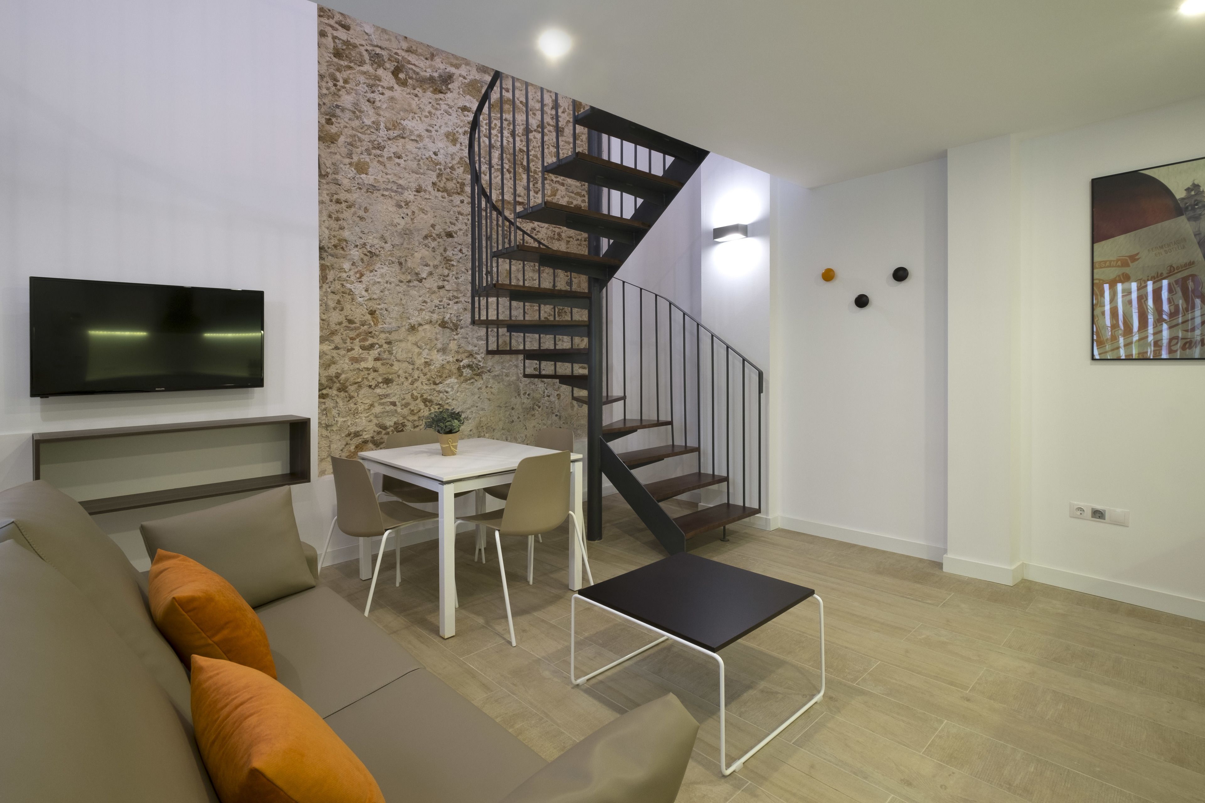 En moderne stue med sofa, et lille bord, fjernsyn og en spiraltrappe.