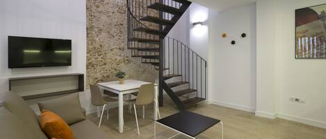 A modern living room with a sofa, a small table, a TV, and a spiral staircase.