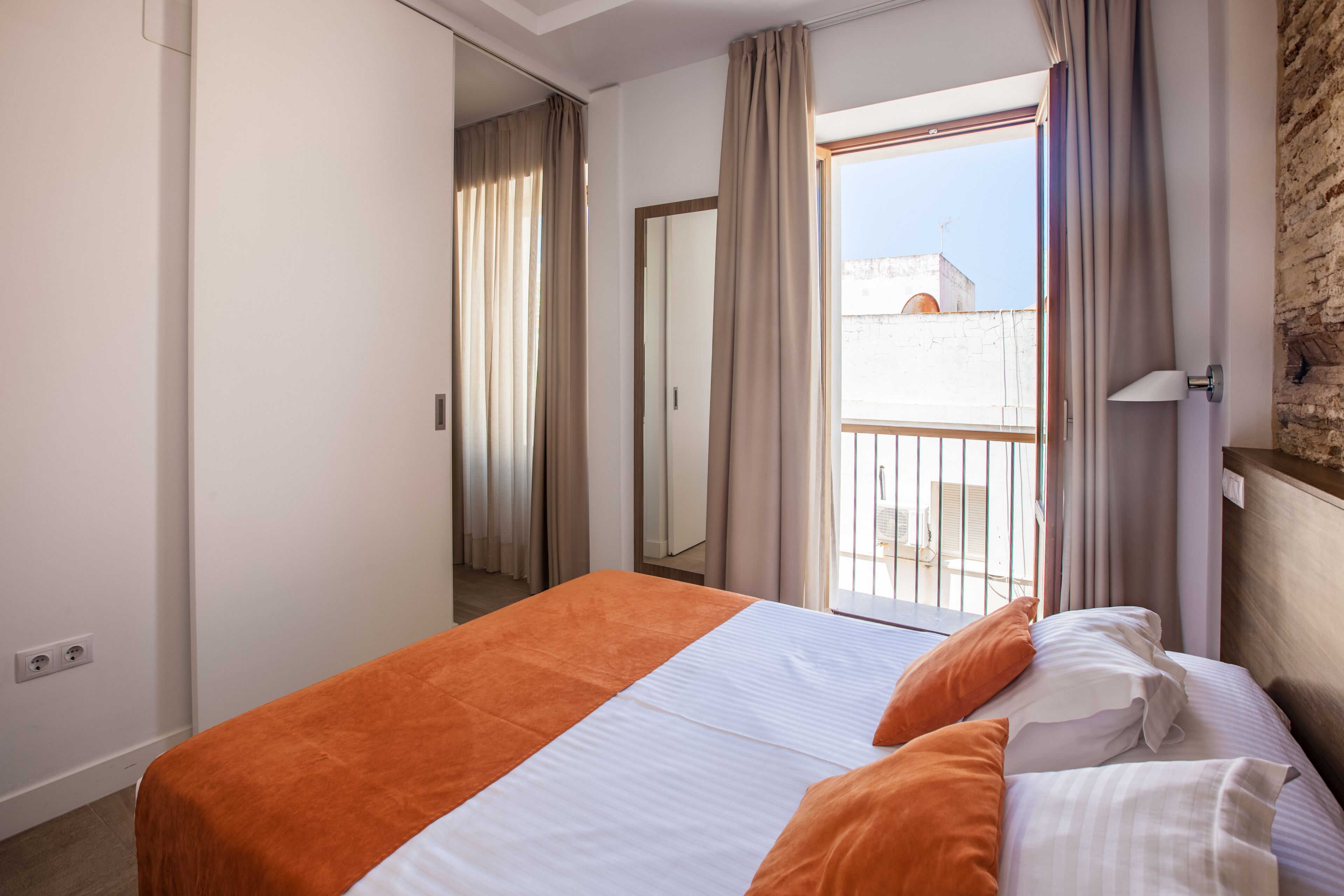 A hotel room with a bed, a window with curtains, a balcony, and a brick wall.