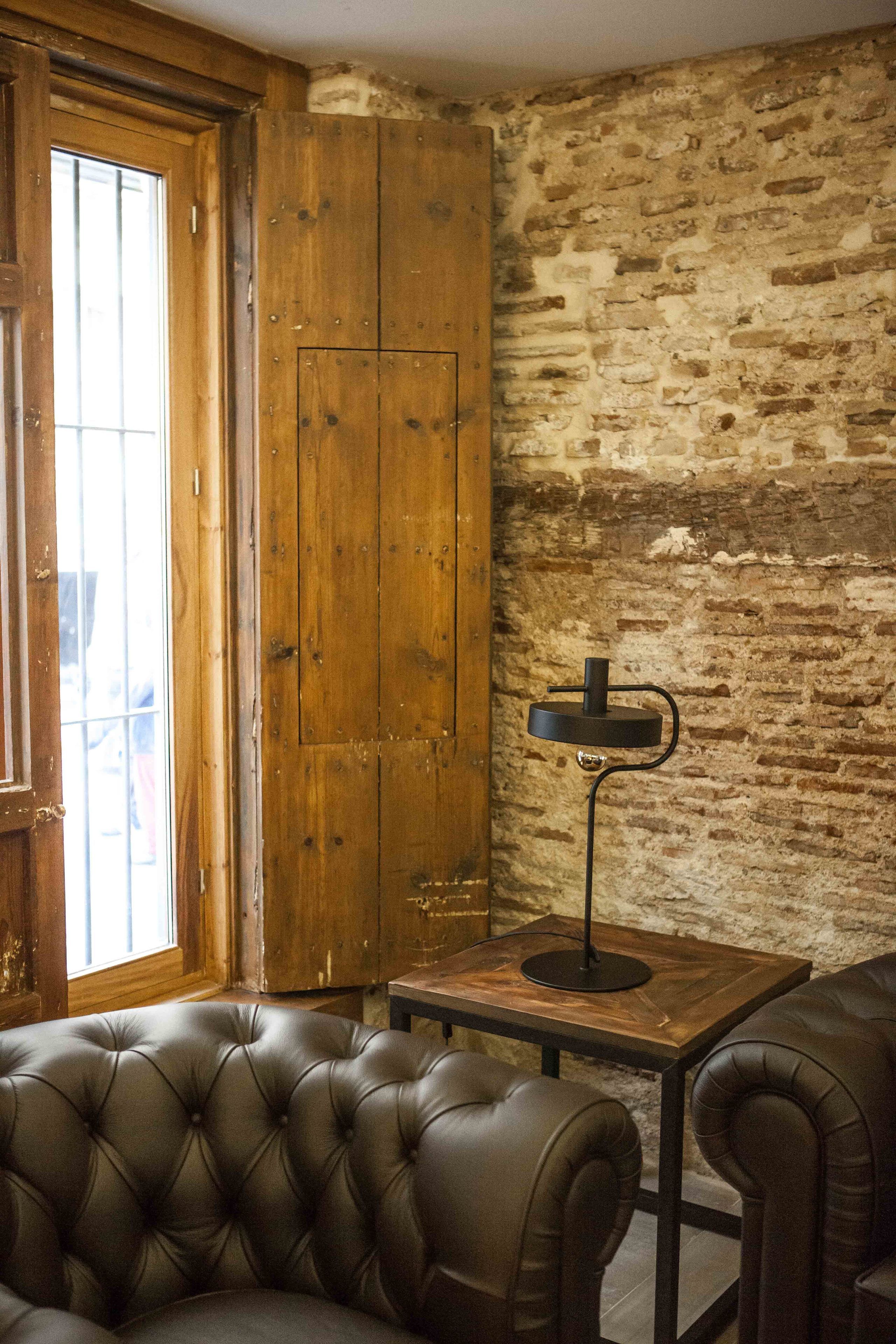 A room with a wooden door, a brick wall, a leather sofa, and a small table with a lamp.