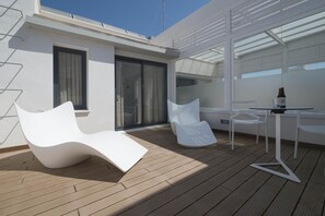 A modern outdoor deck with white furniture, including a lounge chair and a table with a bottle. - Apartamentos Maier (Cádiz)