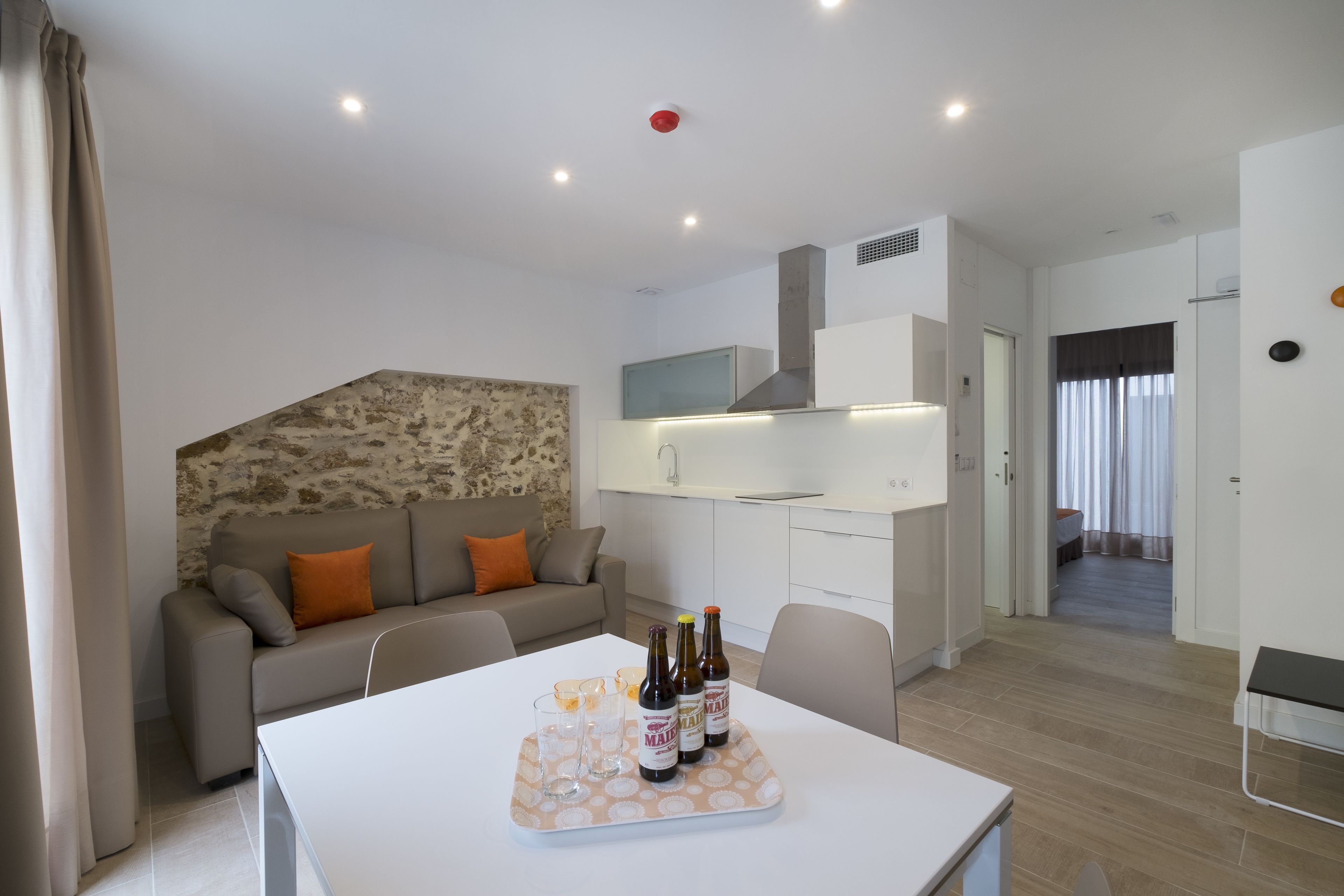 A modern living room with a sofa, a dining table with bottles and glasses, and a kitchen area in the background.