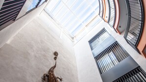 A modern atrium with a high ceiling, a central sculpture, and a view of the sky through the glass. - Apartamentos Maier (Cádiz)