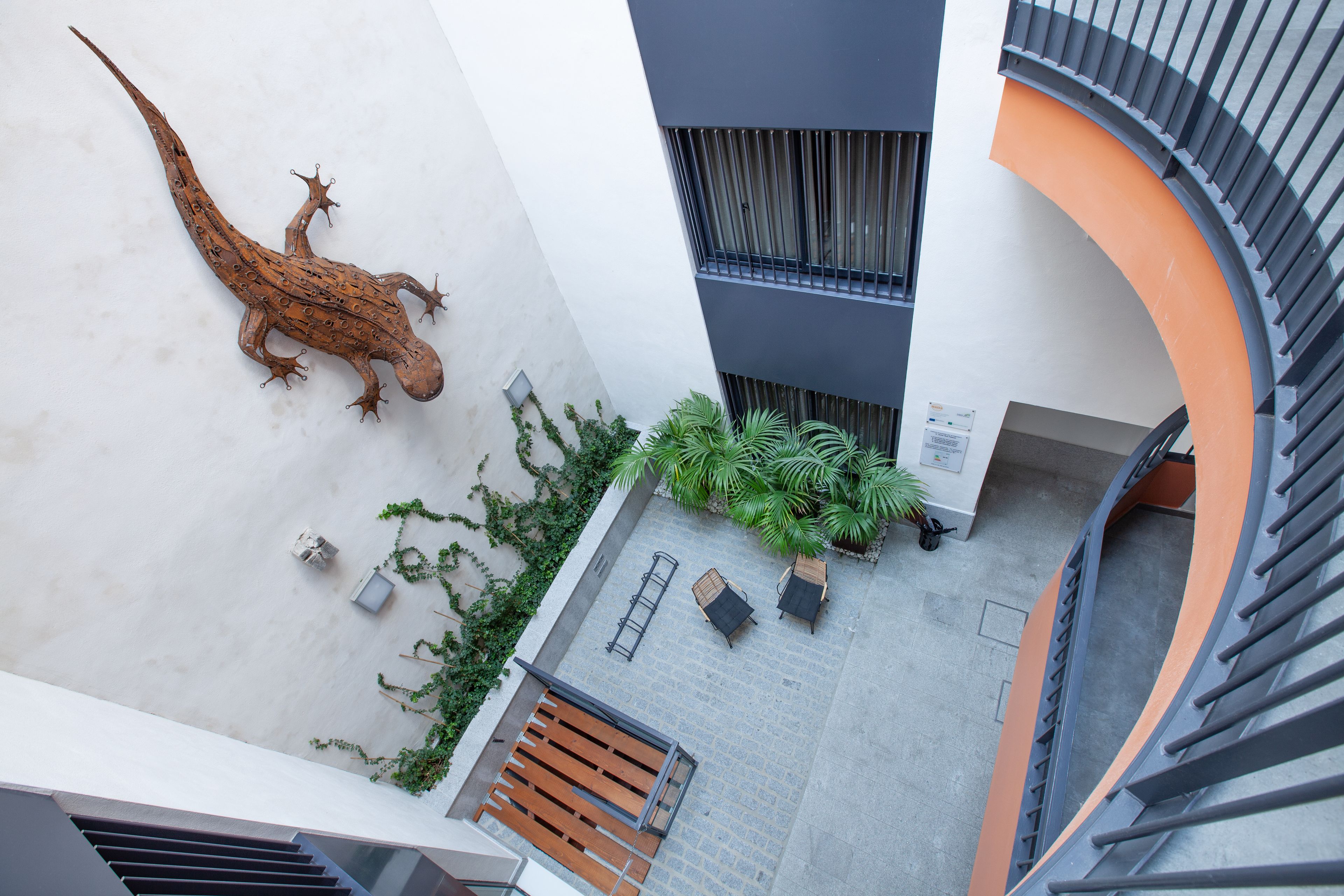A rooftop terrace with a large lizard sculpture, outdoor seating, and a staircase.