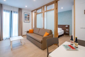 A modern living room with a sofa, a small table, and a chair. There are two bottles on the table. - Apartamentos Maier (Cádiz)