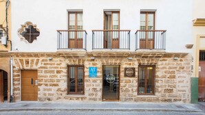 A stone building with a wooden door, a sign for 'AT', and a 'MAIER' sign. - Apartamentos Maier (Cádiz)