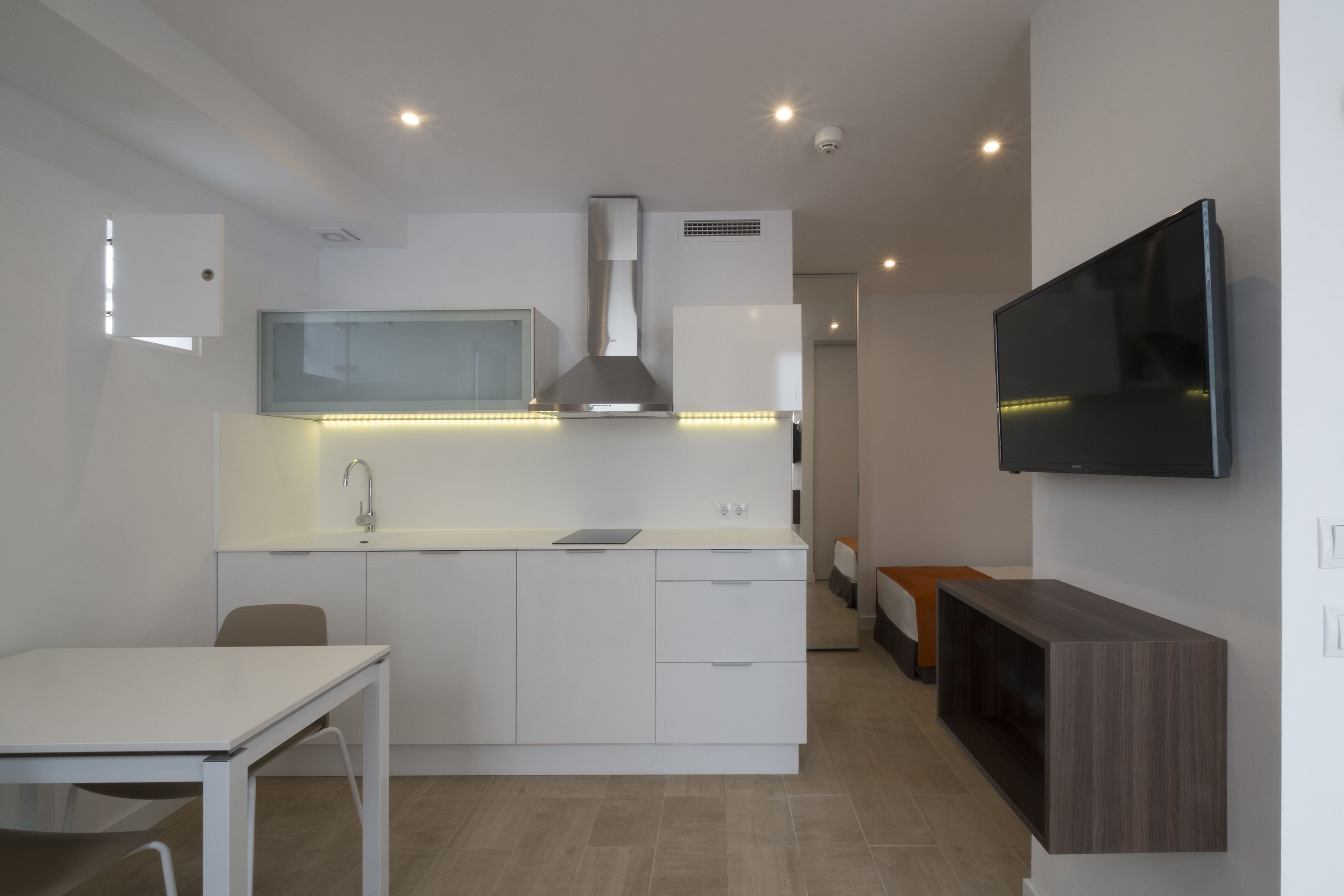 A modern kitchen with white cabinetry, a built-in microwave, and a flat-screen TV mounted on the wall.