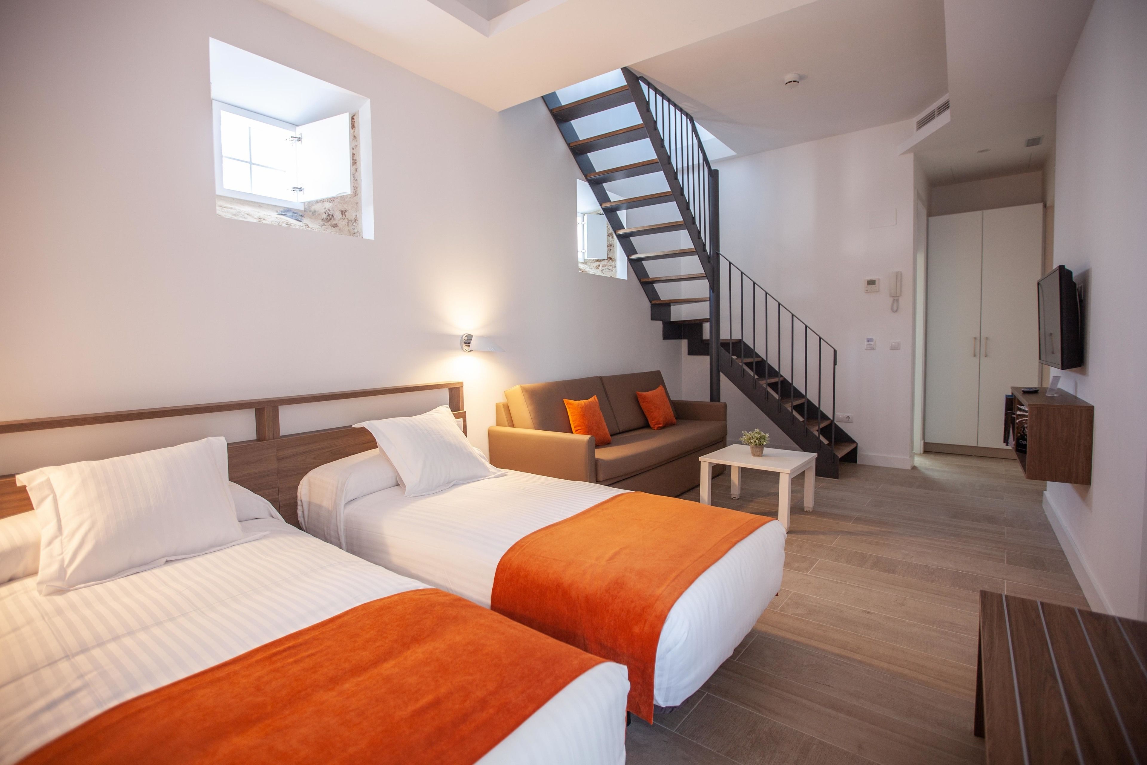 Una habitación de hotel moderna con dos camas, un sofá, una mesita, una escalera y un televisor.