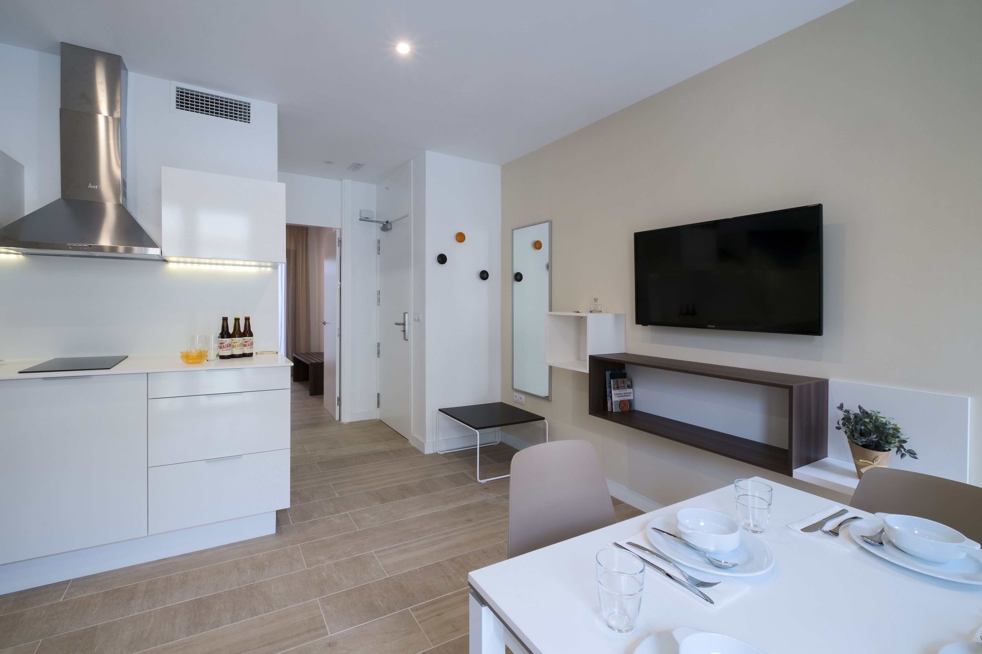 A modern kitchen with white cabinetry, a stainless steel range hood, and a dining area with a white table set for four.