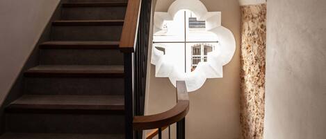 A staircase with wooden steps and a black railing, leading to a landing with a textured wall and a circular window.