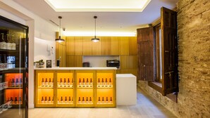 A modern kitchen with wooden cabinets, a central island with bottles, pendant lighting, and a stone wall. - Apartamentos Maier (Cádiz)