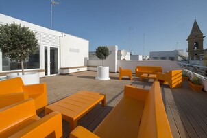 A rooftop terrace with orange seating, a white building, and a clock tower in the background.