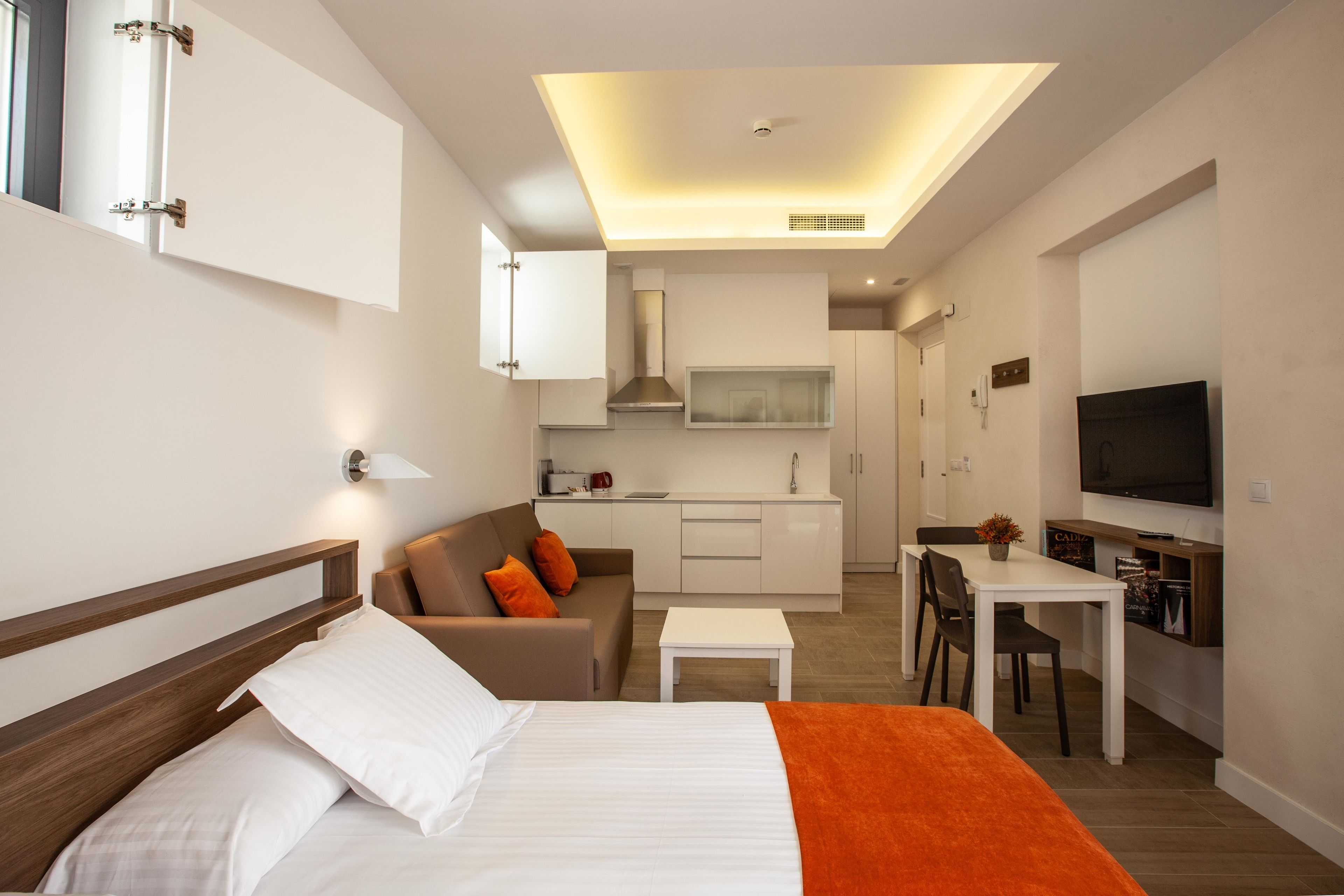Una habitación de hotel moderna con cama, sofá, mesa de comedor y kitchenette.