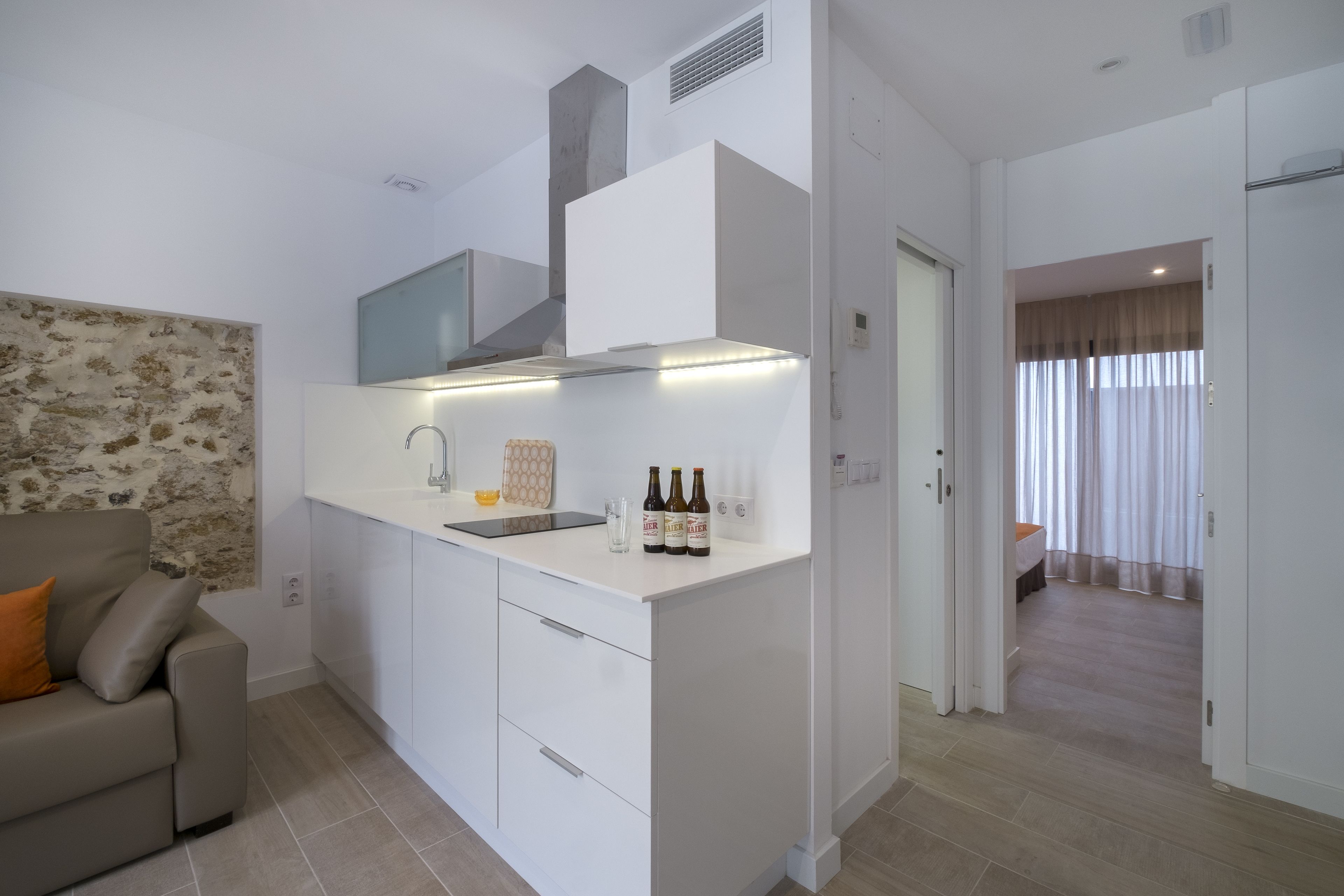 Una cocina compacta con horno integrado, encimera blanca y un lavamanos pequeño. Hay tres botellas de cerveza sobre la encimera.
