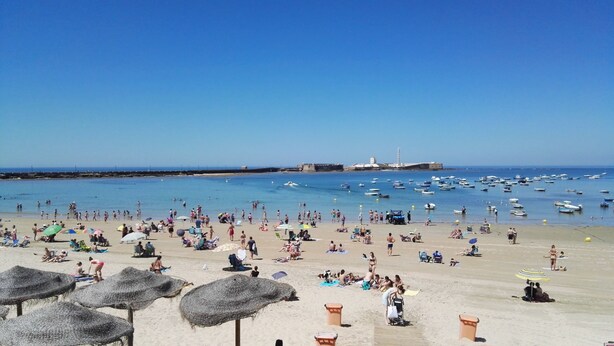 A beach with umbrellas, sun loungers, and people relaxing. - Apartamentos Maier (Cádiz)