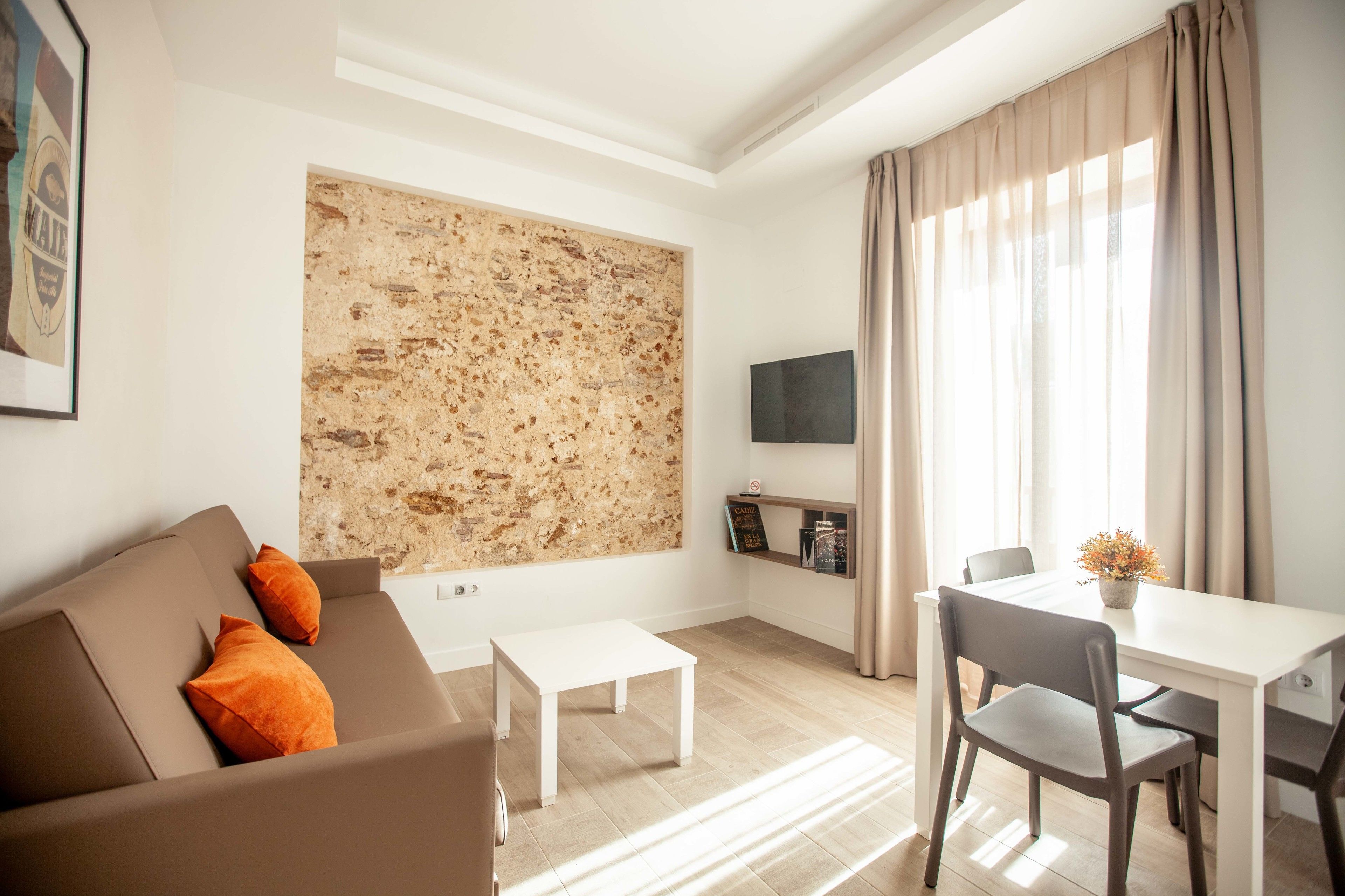 Un salon moderne comprenant un canapé, une petite table, une table à manger avec des chaises, un téléviseur à écran plat et un grand mur à texture.